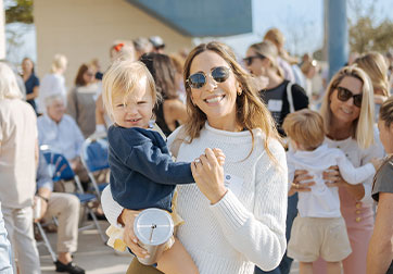 Photo of a woman with sunglasses holding child. Links to Gifts of Life Insurance page.